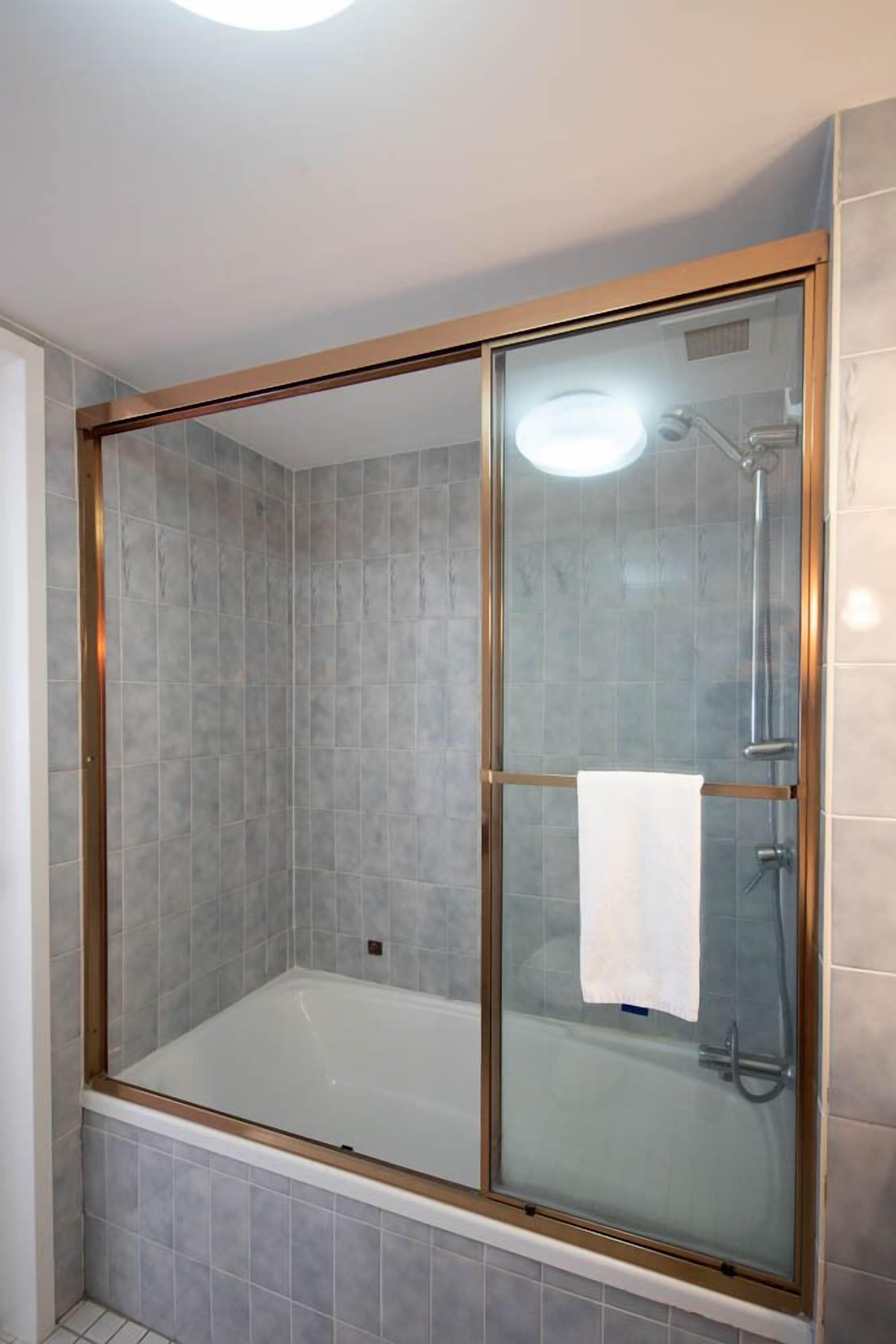 Una ducha a ras de suelo con puerta de cristal, azulejos grises y una toalla blanca colgada en la puerta.