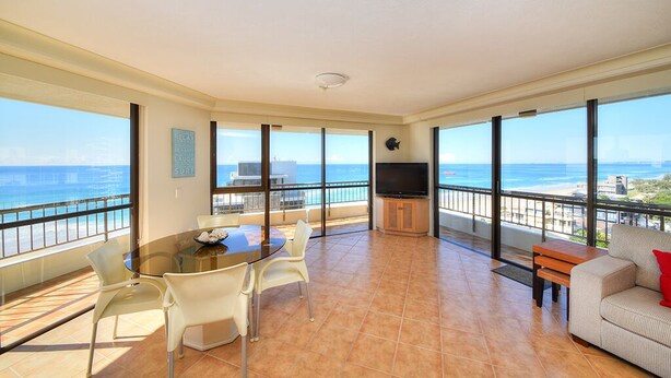 A spacious balcony with a view of the sea, a dining area with chairs and a table, and a TV on a wooden cabinet. - Bougainvillea Luxury Apartments (Main Beach)