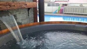 A hot tub with water flowing into it, surrounded by a stone wall and a wooden deck. - Cosy Corner Holiday Park (Tauranga)