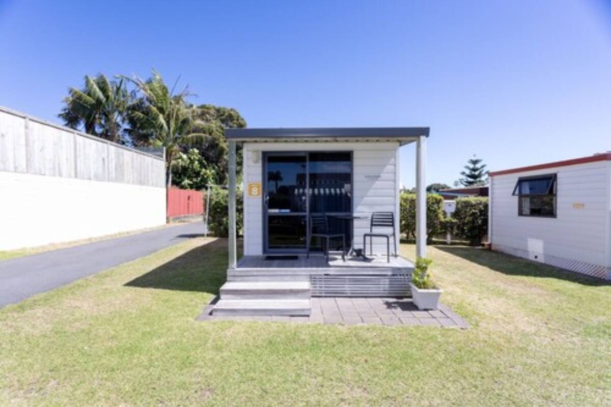 A modern, single-story building with a covered outdoor seating area, a small entrance, and a paved driveway.