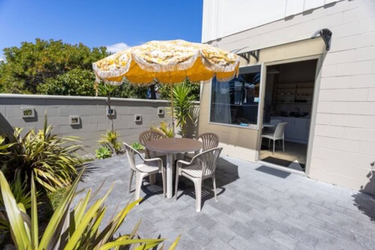 An outdoor patio with a round table and chairs, a yellow umbrella, and a glass door leading to a room.