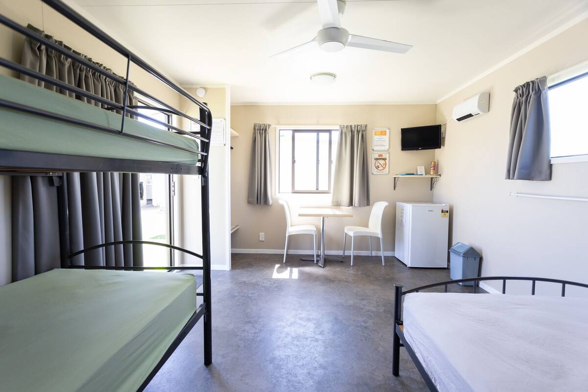 A dormitory room with bunk beds, a desk, a chair, a small fridge, and a television.