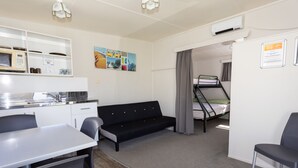 A compact room with a kitchenette, a sofa, a bunk bed, and a dining area. - Cosy Corner Holiday Park (Tauranga)