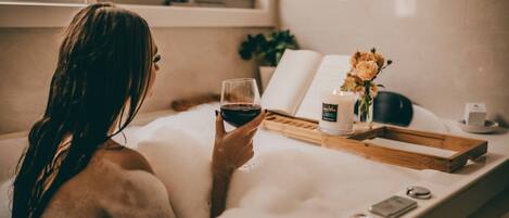 A person in a bathtub with a book and a glass of wine.