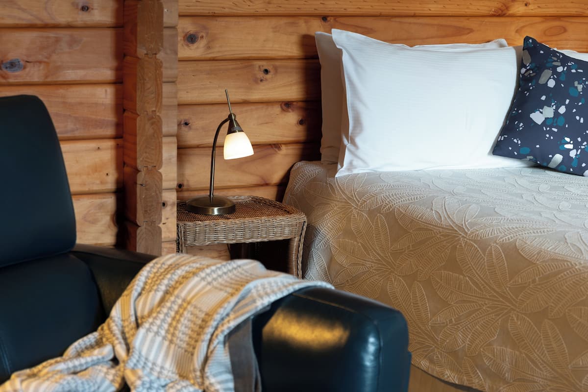 A cozy room with a bed, a chair, a lamp, and a small table.