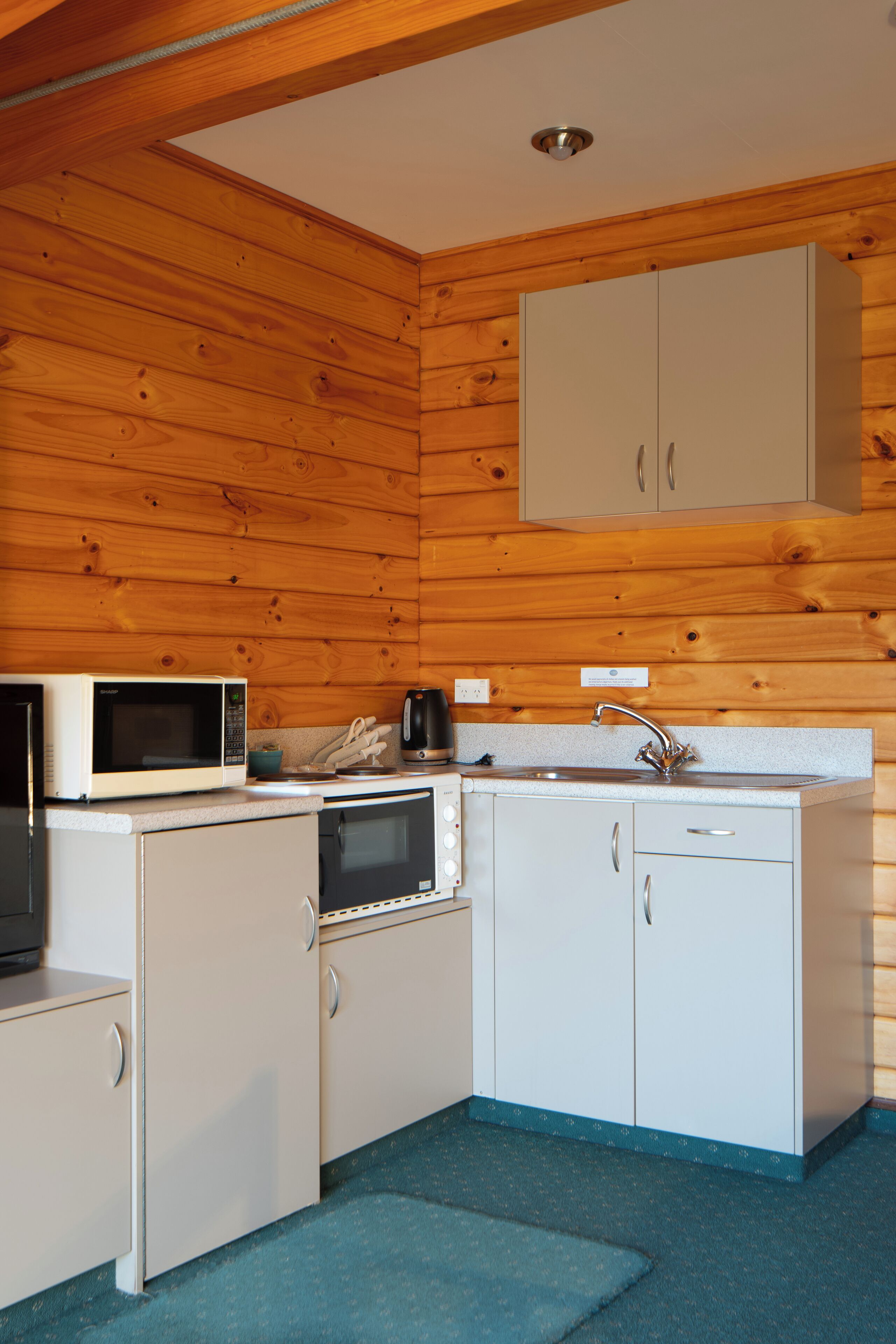 Une cuisine compacte avec des murs en bois, des meubles blancs, un four à micro-ondes, une machine à café et un évier.
