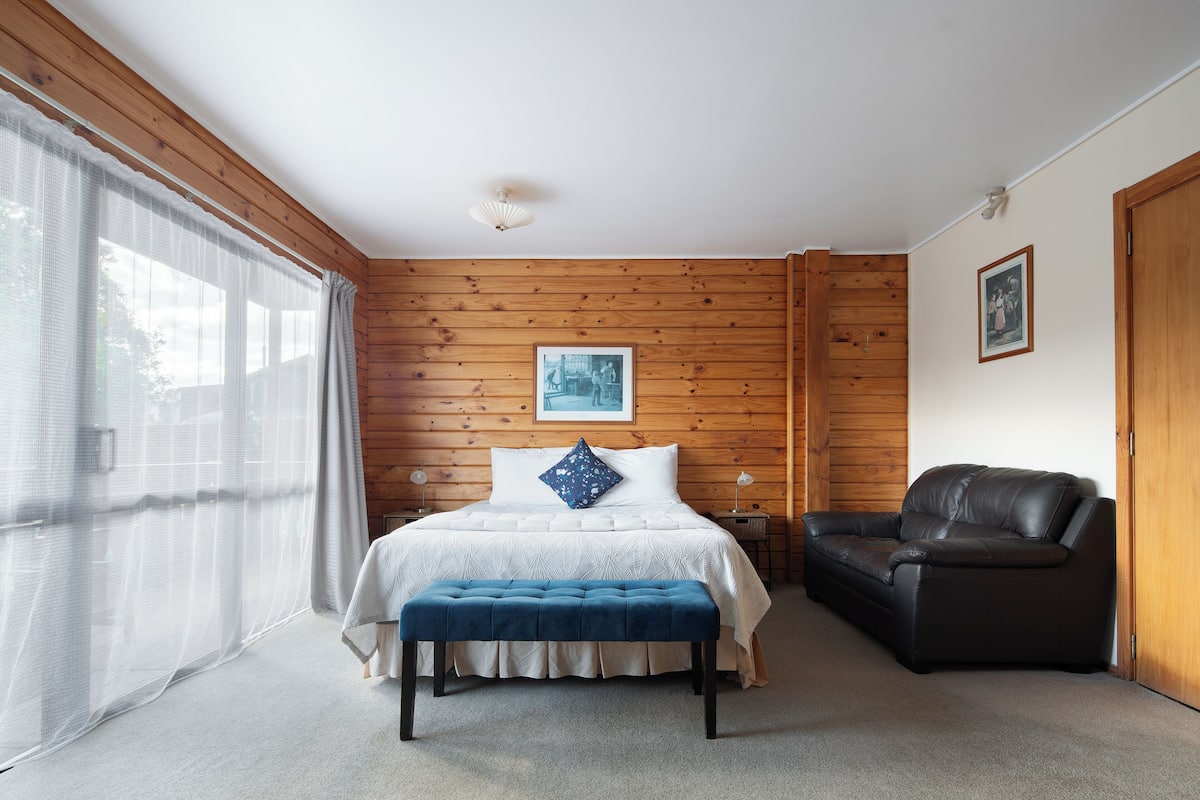 A bedroom with a bed, bench, and a black leather sofa.