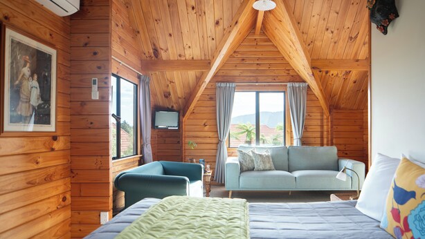 A cozy wooden cabin room with a bed, a sofa, and a TV. - Fox Glacier Lodge (Fox Glacier)