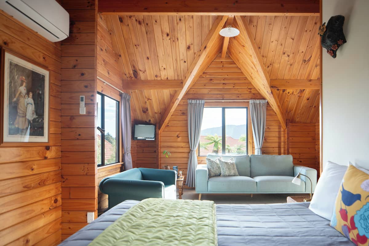 A wooden cabin room with a bed, a sofa, and a TV.