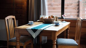 A wooden dining table with a woven placemat, two chairs, a basket of bread, a teapot, a cup, and a glass of water. - Fox Glacier Lodge (Fox Glacier)