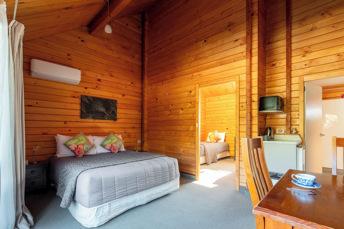 A wooden cabin room with a bed, a table with a cup, and a television.