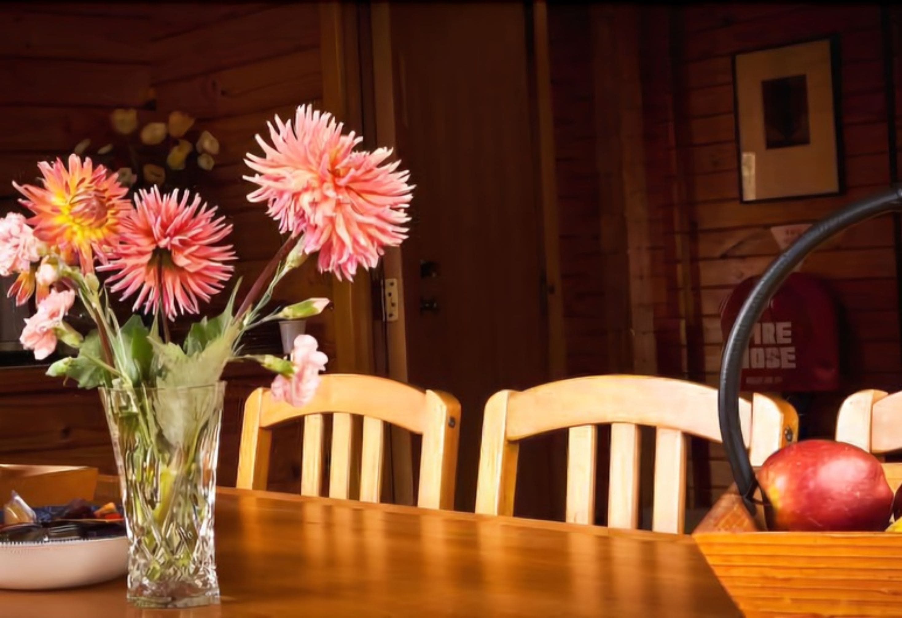 A wooden dining table with a clear glass vase containing pink flowers.