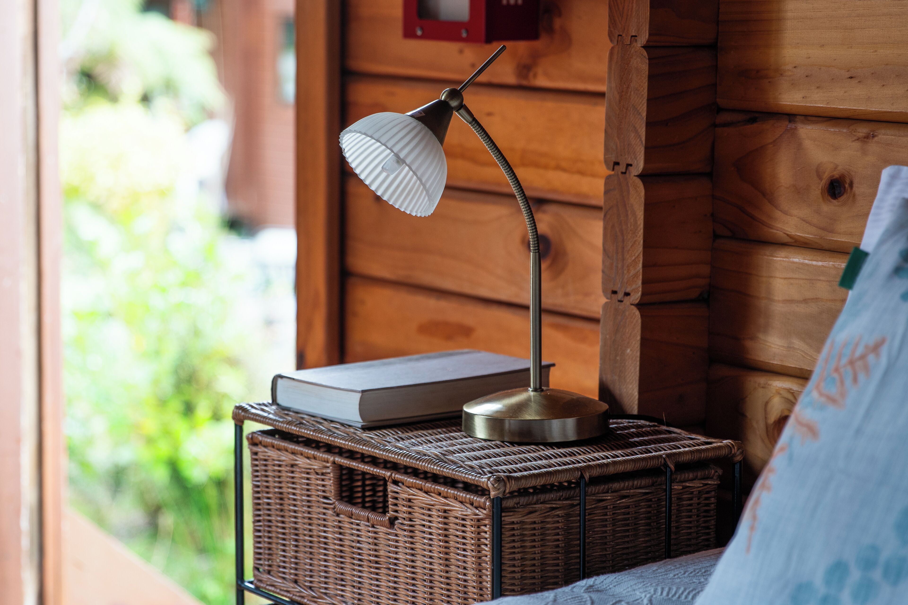 Ein Korbwäscher mit einer Lampe und einem Buch an einer Holzwand.