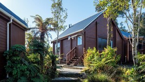 A wooden house with a staircase leading to the entrance, surrounded by lush greenery. - Fox Glacier Lodge (Fox Glacier)