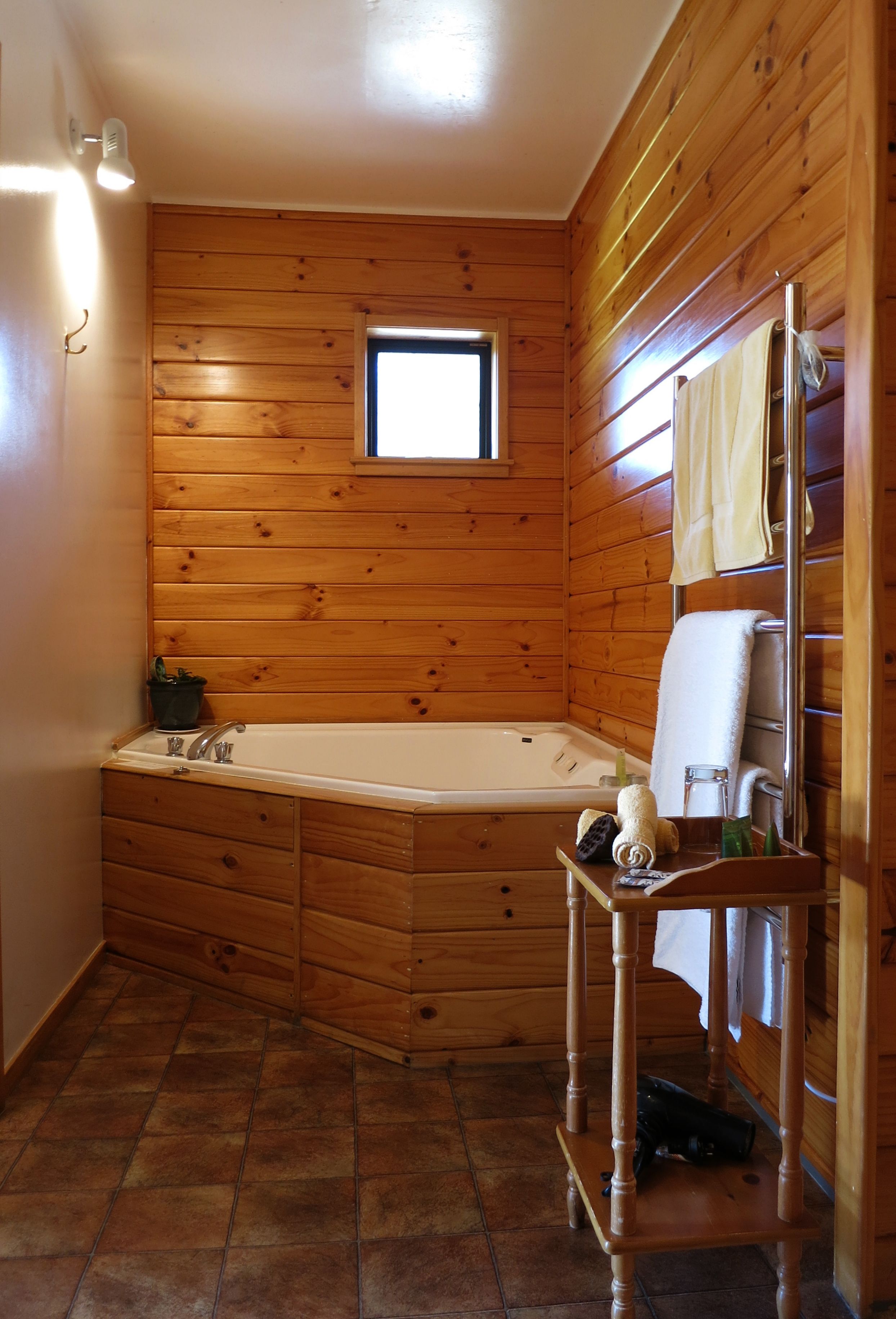 Un baño de cabaña de madera con una bañera, un ventanal pequeño y un perchero para toallas.