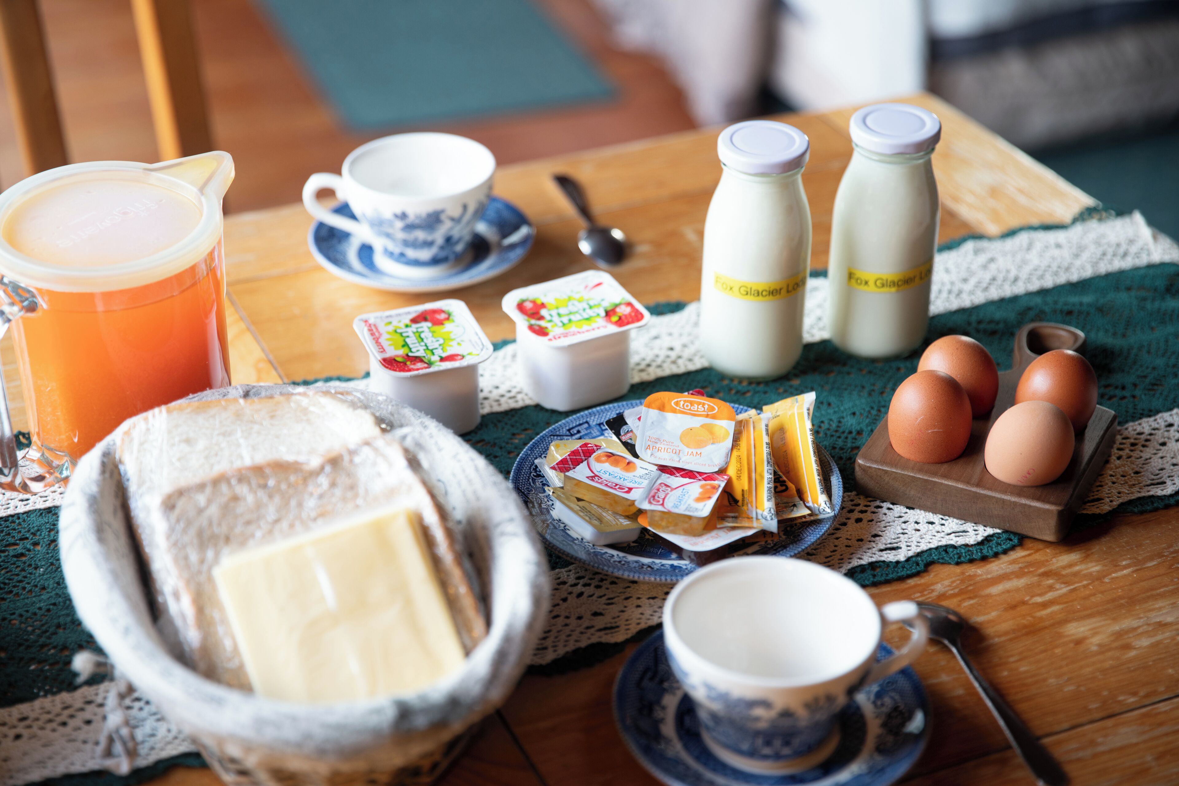 Una mesa de desayuno con tostadas, mantequilla, huevos, leche y una taza de café.