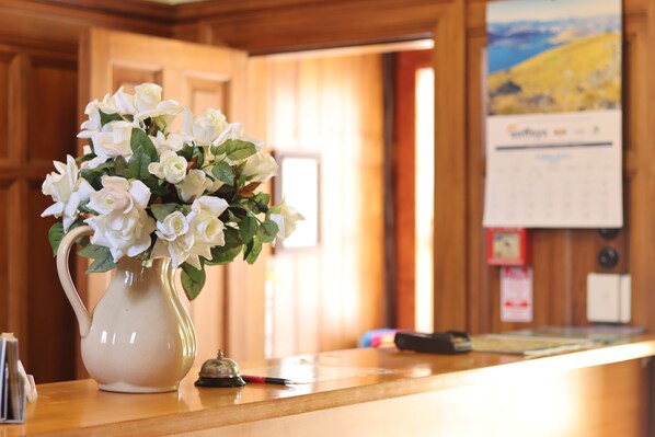 A white ceramic pitcher with white roses on a wooden counter in a room with wooden paneling and a calendar on the wall.