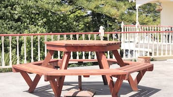 A wooden picnic table with a bench, surrounded by a white fence and greenery.