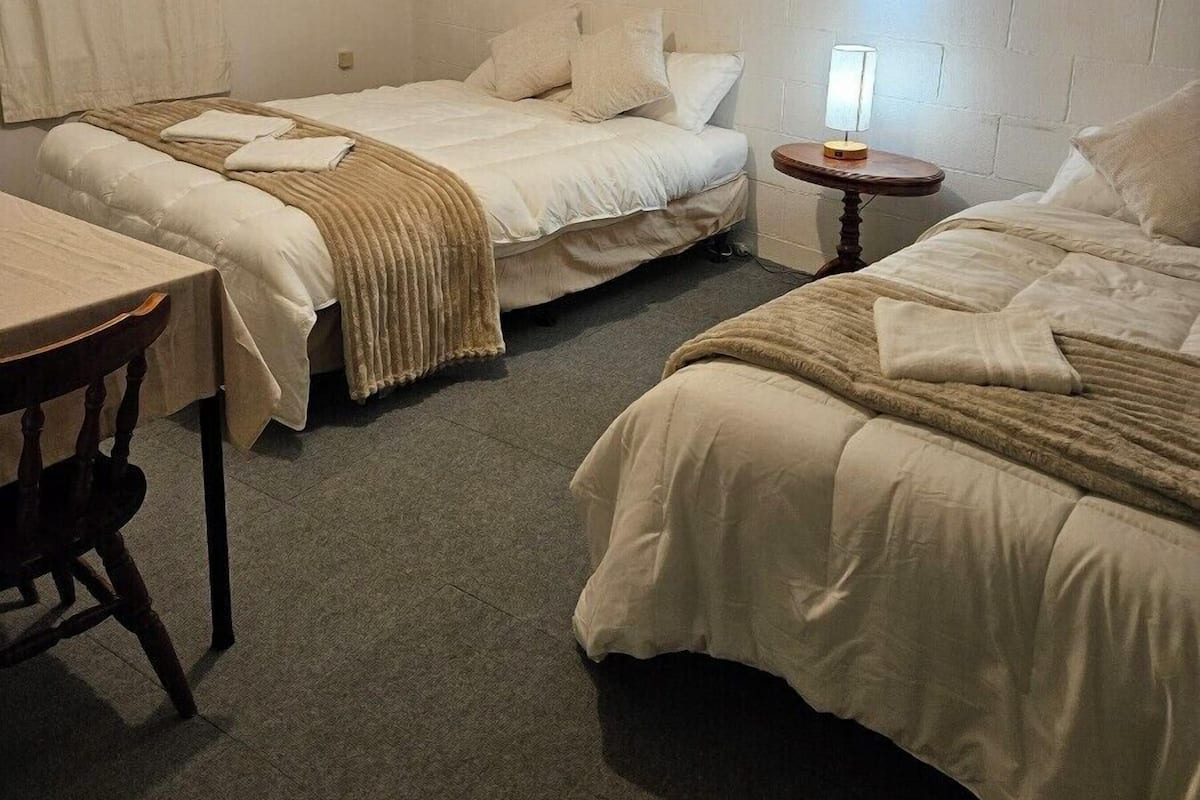 Quarto com três camas, uma mesa e uma luminária.
