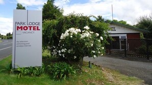 Letrero del motel Park Lodge, con aviso de habitaciones disponibles, rodeado de abundante vegetación y una cerca.
