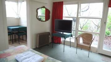 Ein Hotelzimmer mit einem Bett, einem Schreibtisch mit Fernseher, einem Sessel und einem Fenster mit Blick auf Bäume.