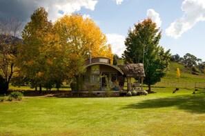 A rustic cabin with a curved roof, surrounded by a lush garden and autumn-colored trees.