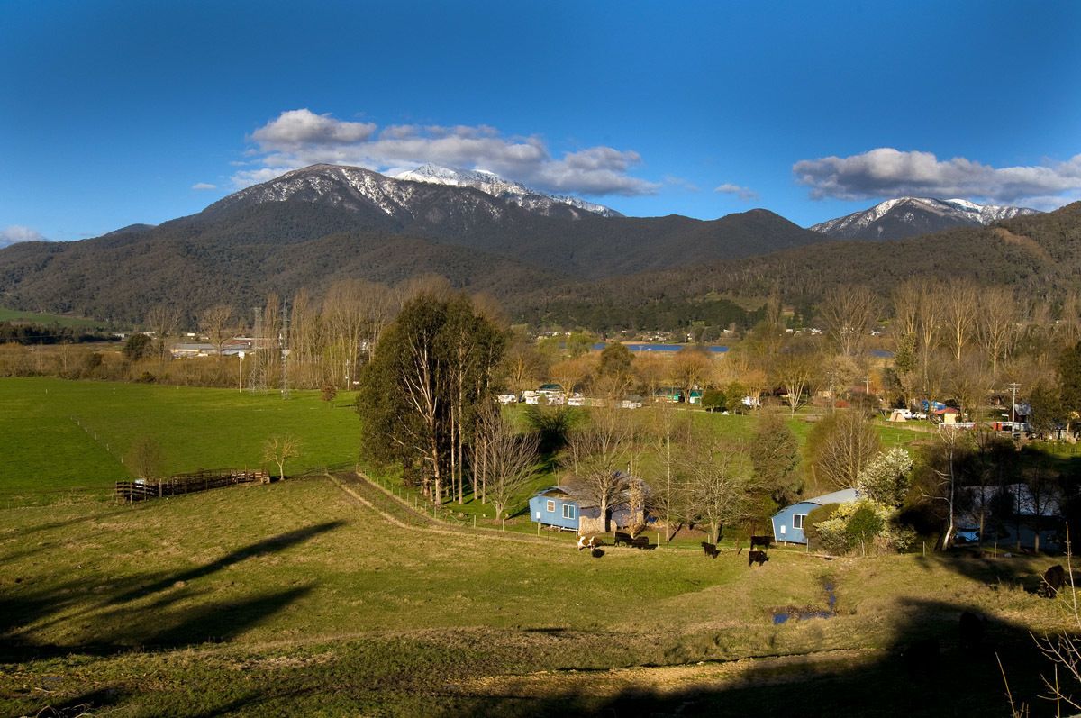 Un paisaje rural con una cadena montañosa, un pequeño pueblo y una masa de agua.
