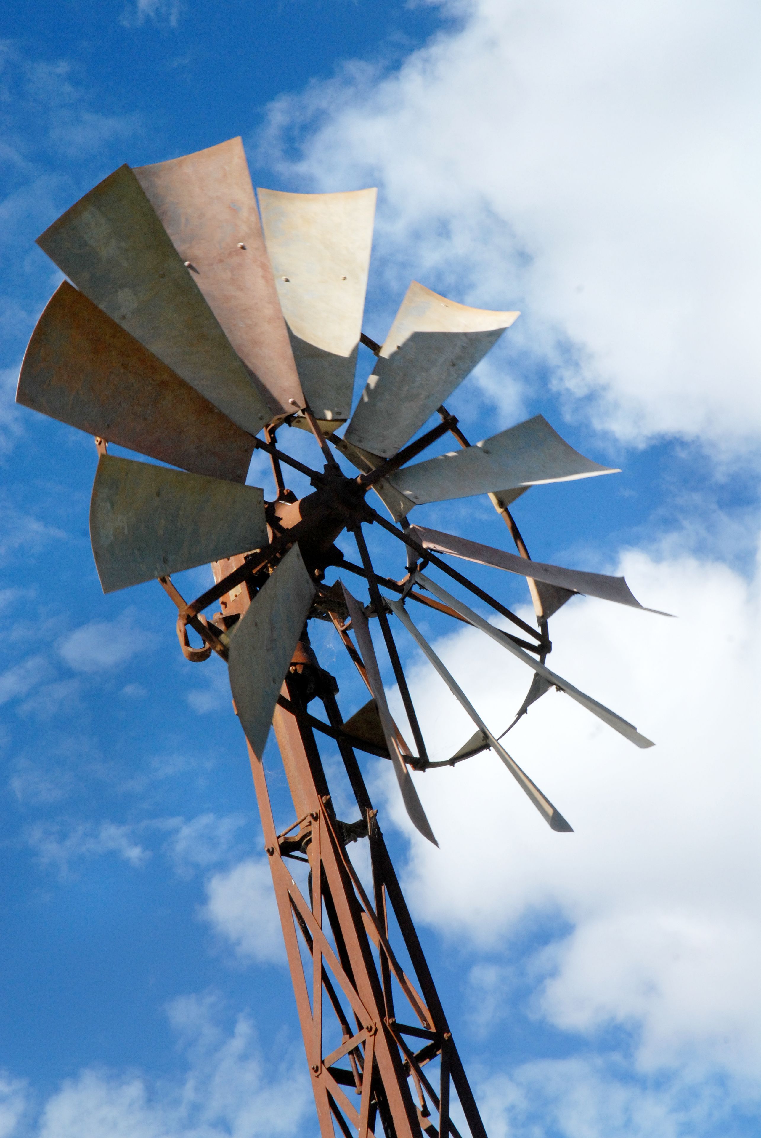 A windmill with multiple blades against a blue sky with clouds.