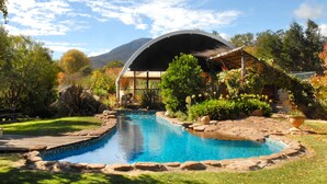 A swimming pool with a wooden deck, surrounded by lush greenery and a mountain in the background. - Dreamers (Tawonga South)