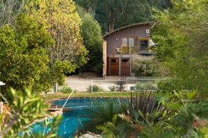 A modern house with a pool, surrounded by lush greenery and a white fence.