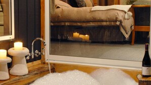 A room with a large window, a bathtub filled with bubbles, and a bottle of wine on a wooden table. - Dreamers (Tawonga South)