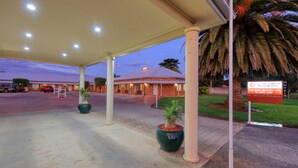 Un motel doté d’un parking couvert, d’un panneau indicateur et d’un palmier.