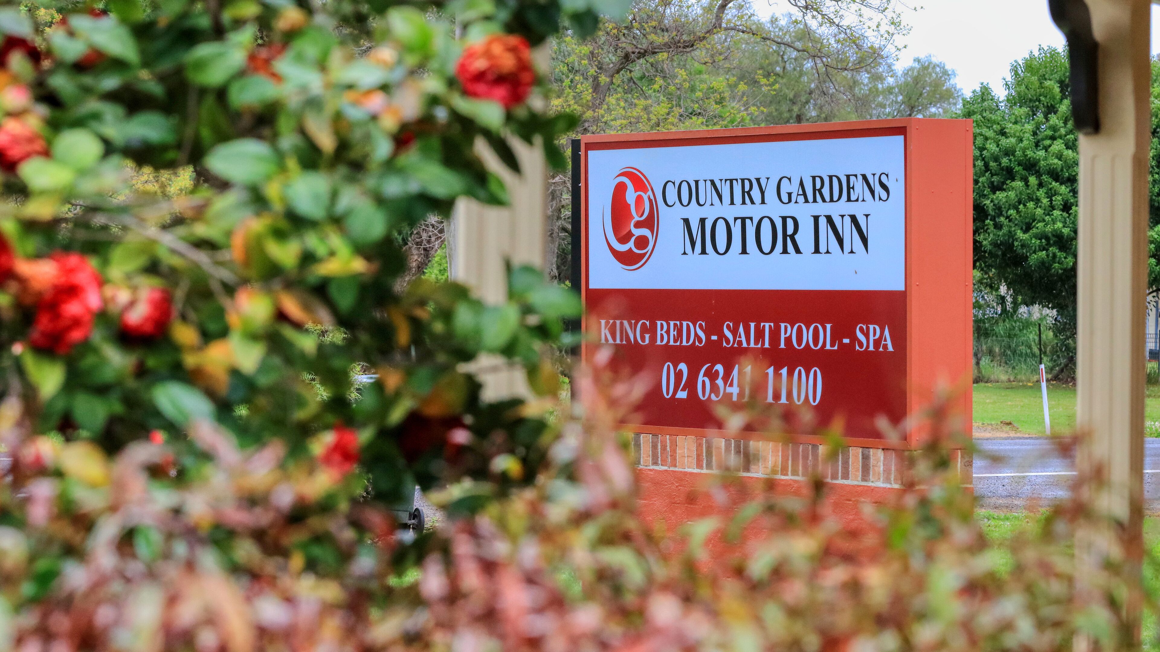 Señal del Motor Inn Country Gardens que indica servicios como camas extragrande, piscina con agua salada y spa.