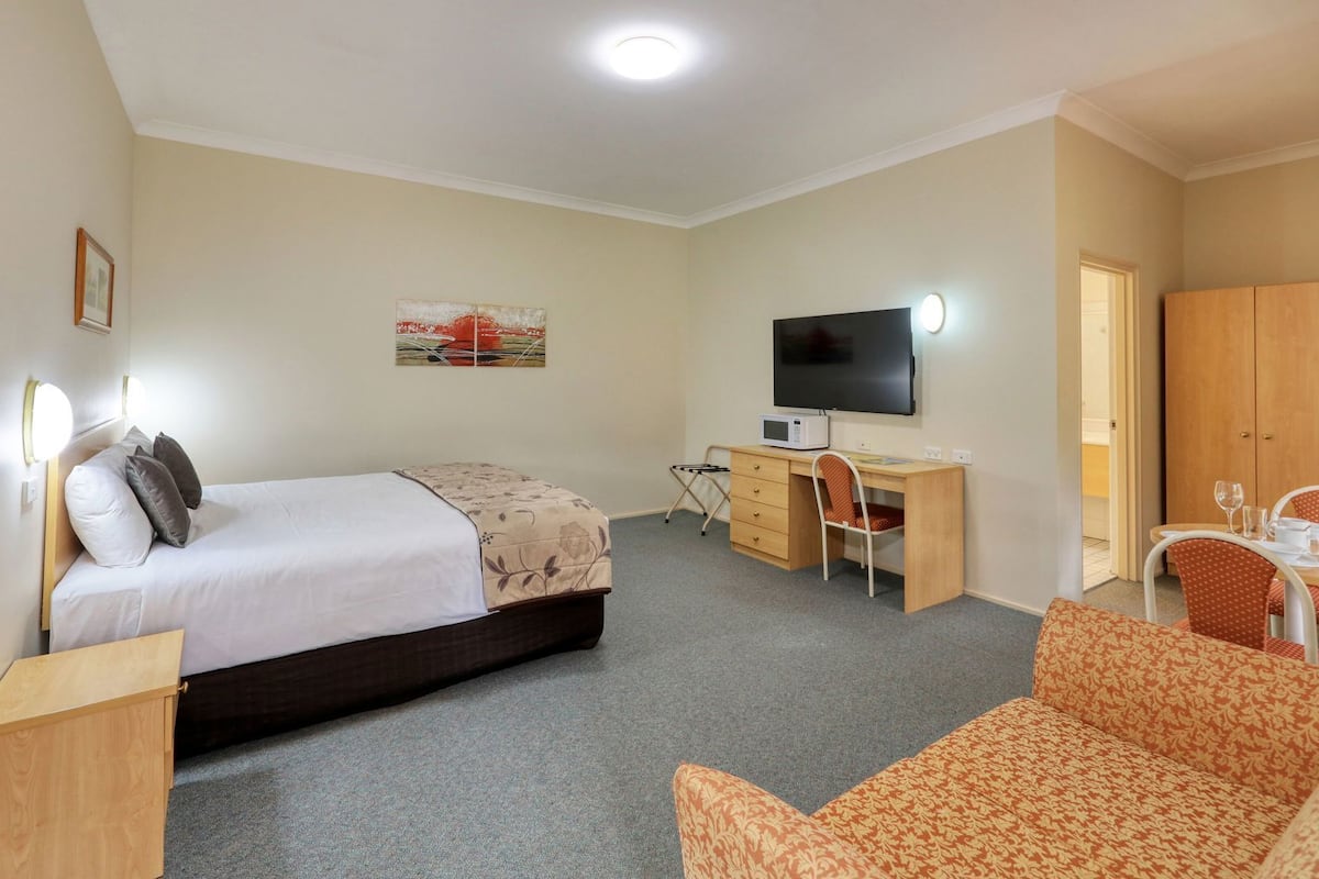 Habitación de hotel con cama, escritorio con computadora, televisor, zona de comedor con sillas y armario.