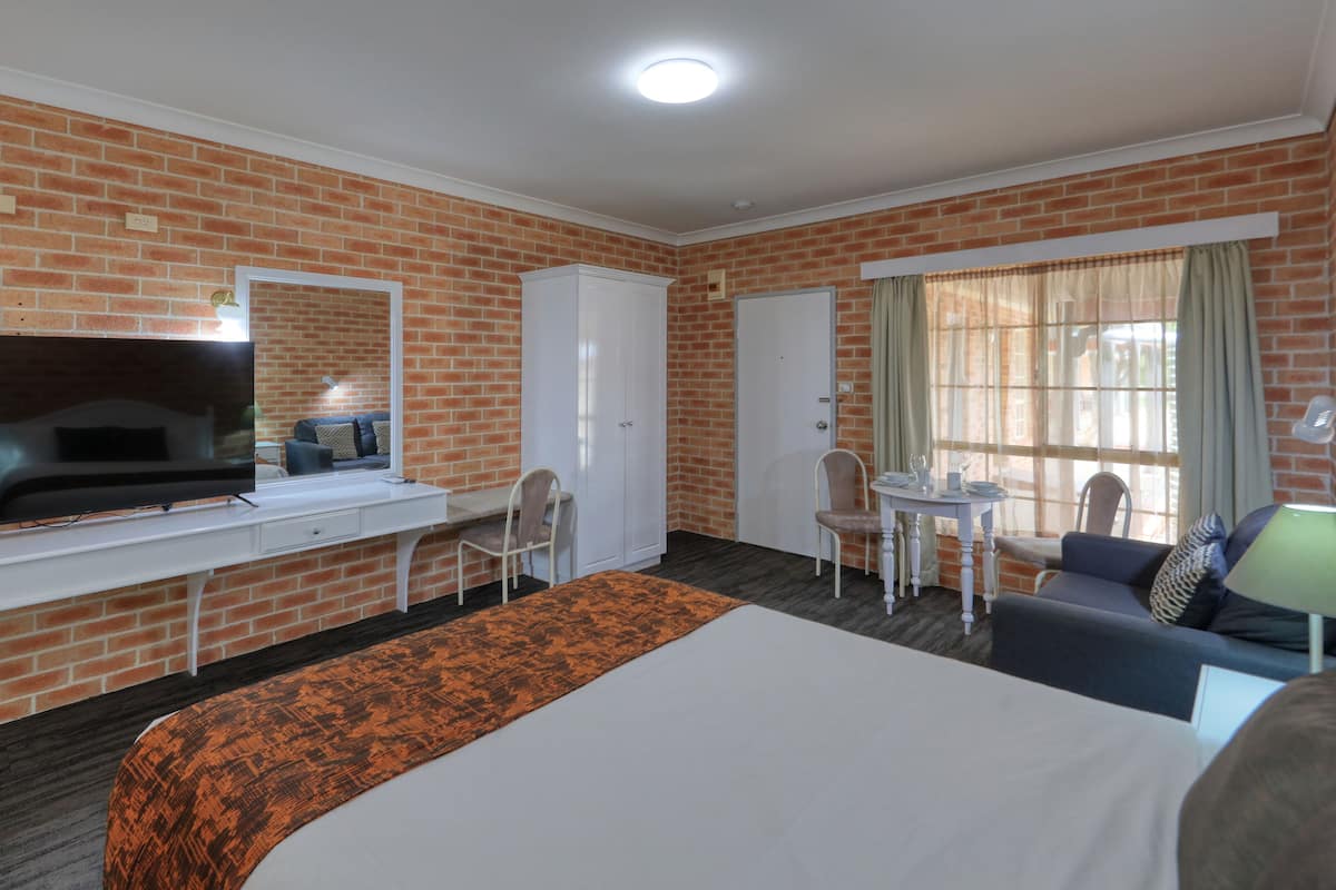 Habitación de hotel con pared de ladrillo, un televisor de pantalla plana, una cama, un escritorio con una silla, una pequeña mesa con sillas y una ventana con cortinas.