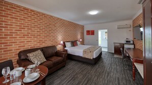 Une chambre d’hôtel avec un mur en briques, un lit recouvert d’une couette blanche, un canapé en cuir marron et une table à manger dressée avec des assiettes, des verres et des couverts.