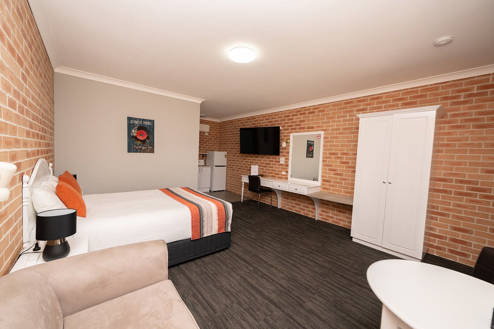 A hotel room with a bed, a desk, a chair, a small table, a mirror, and a wardrobe.