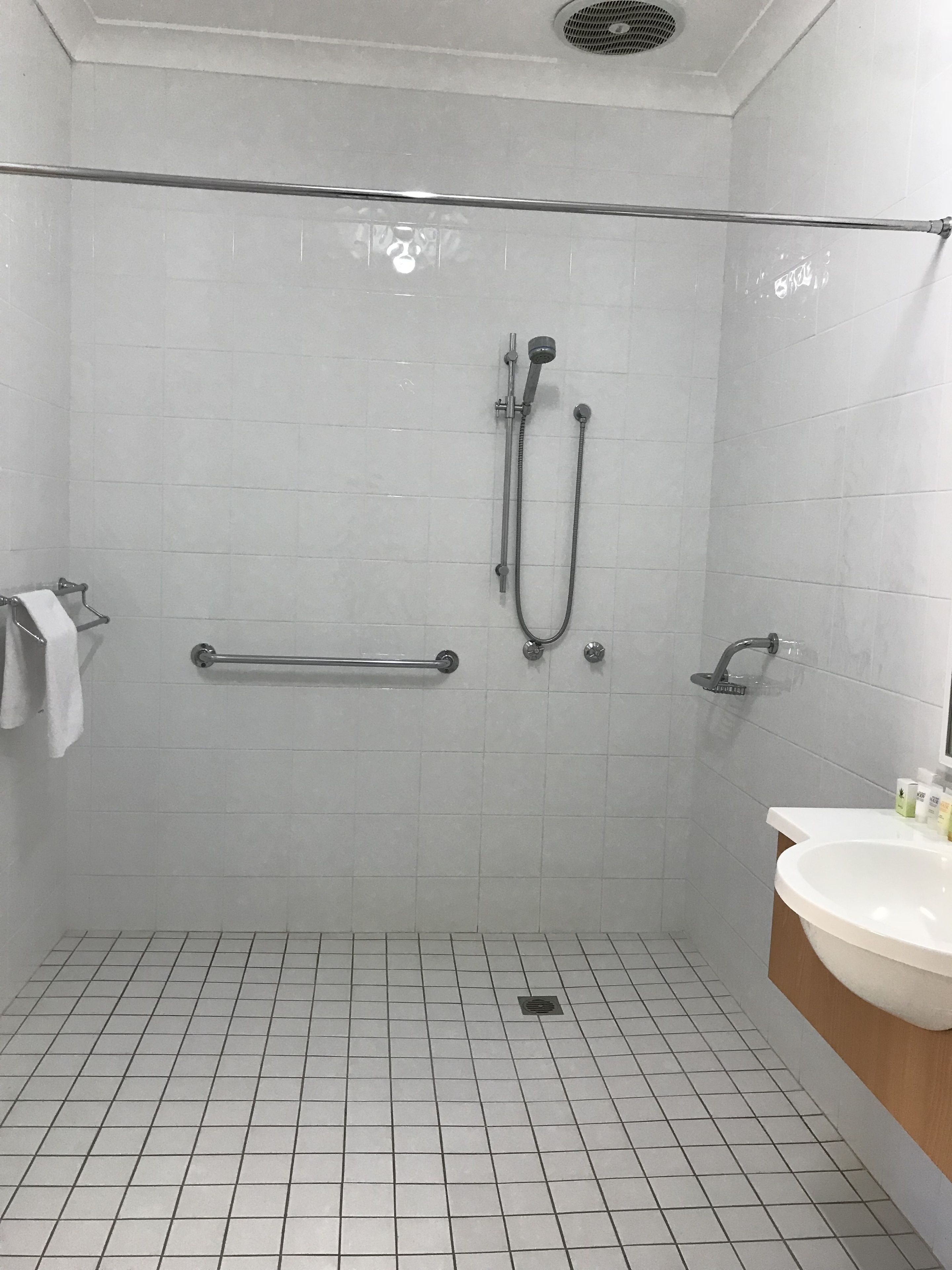 A bathroom with a shower, grab bar, and sink.