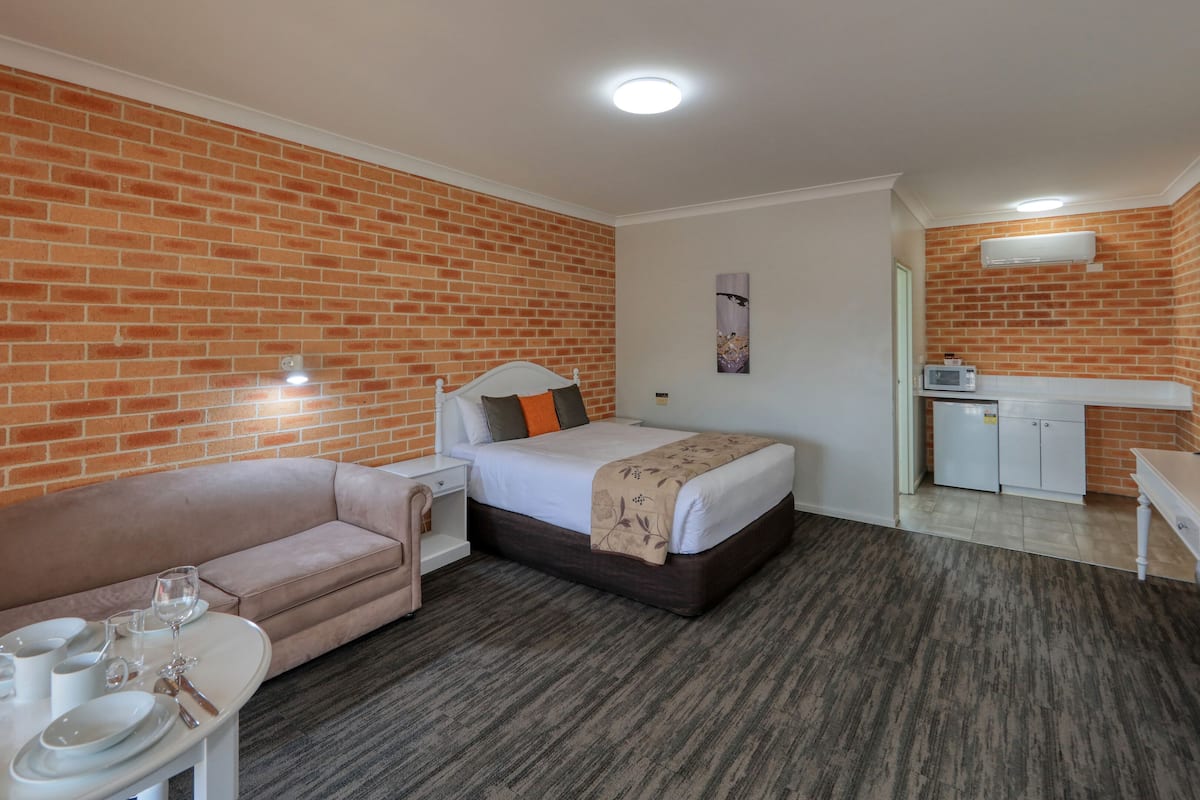 Habitación de hotel con pared de ladrillo, cama, kitchenette pequeña y zona de estar con mesa lista para comer.