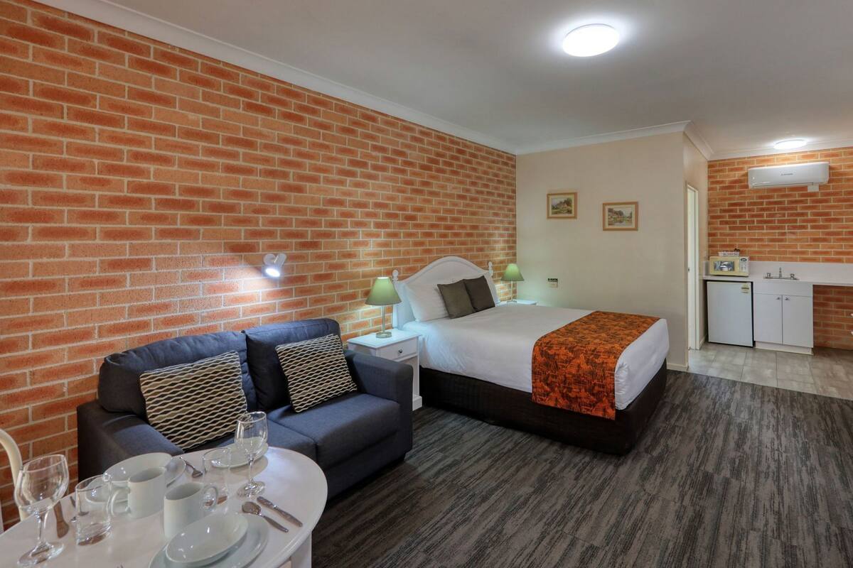 Una habitación de hotel compacta con pared de ladrillo, una cama, una kitchenette pequeña, un área de comedor y un espacio de estar.