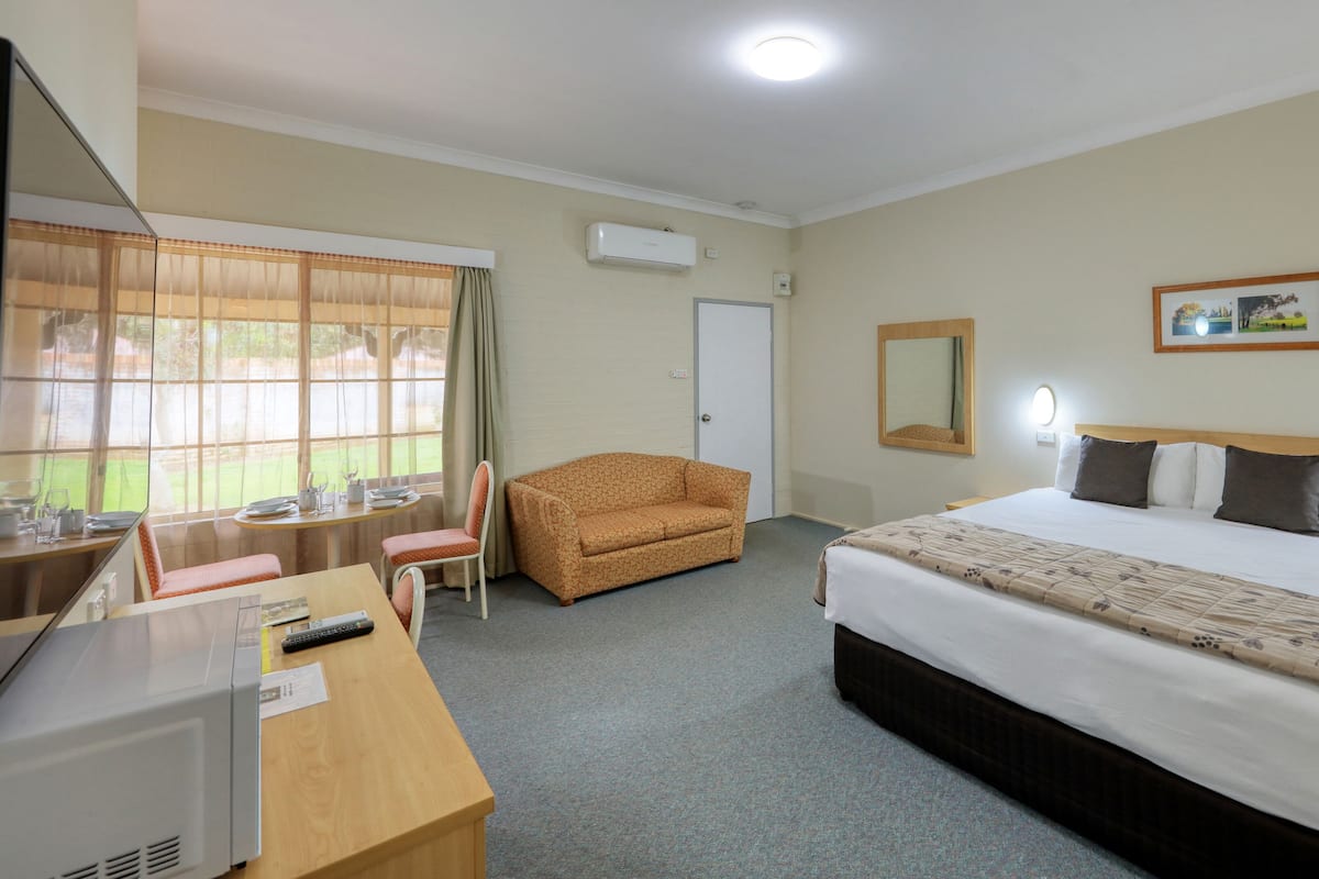 Una habitación de hotel con cama, escritorio, silla, televisor y ventana con cortinas.
