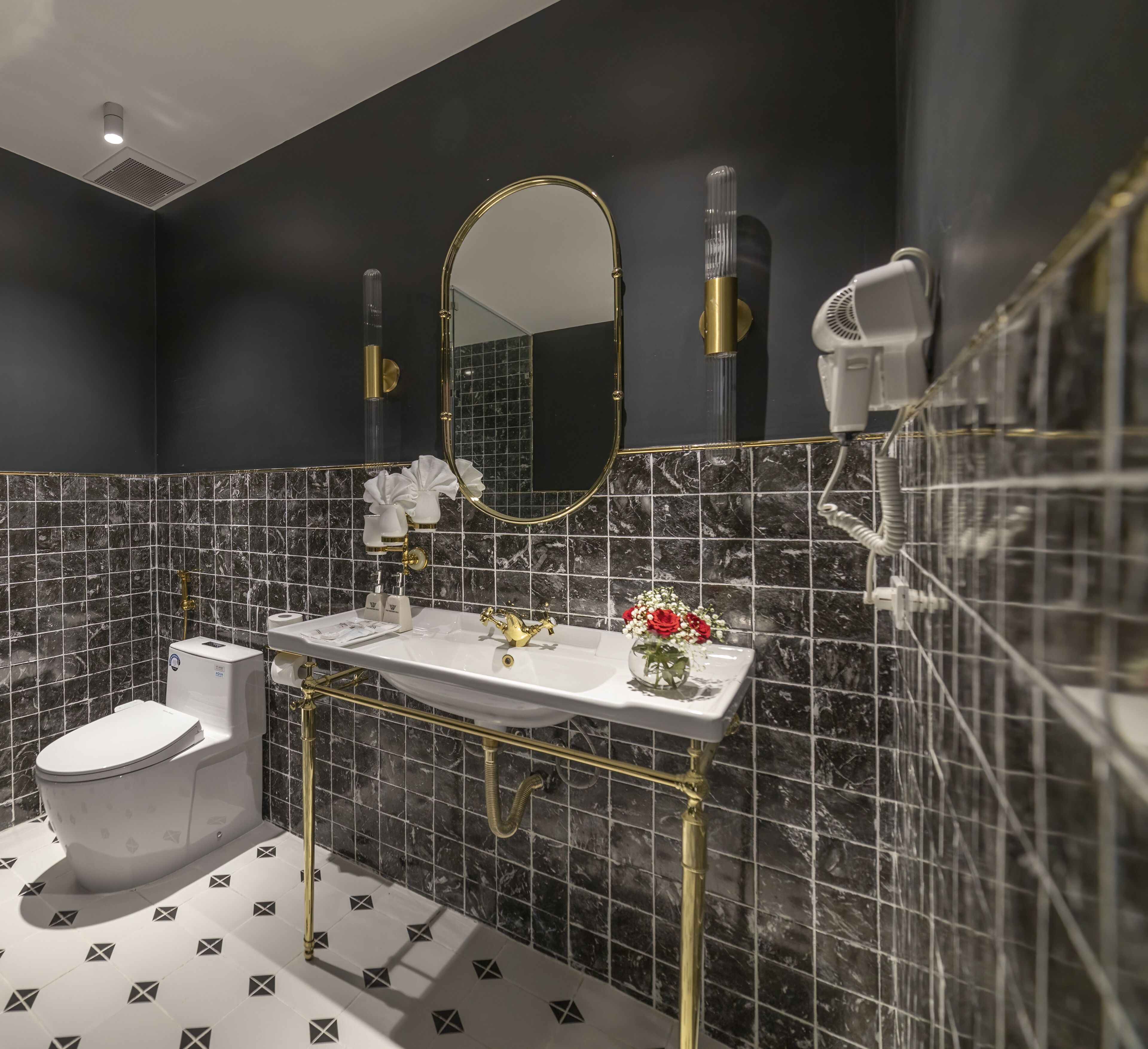 Ein Badezimmer mit einer weißen Toilette, einem goldrahmigen Waschtisch, einem Spiegel und einer Duschkabine.