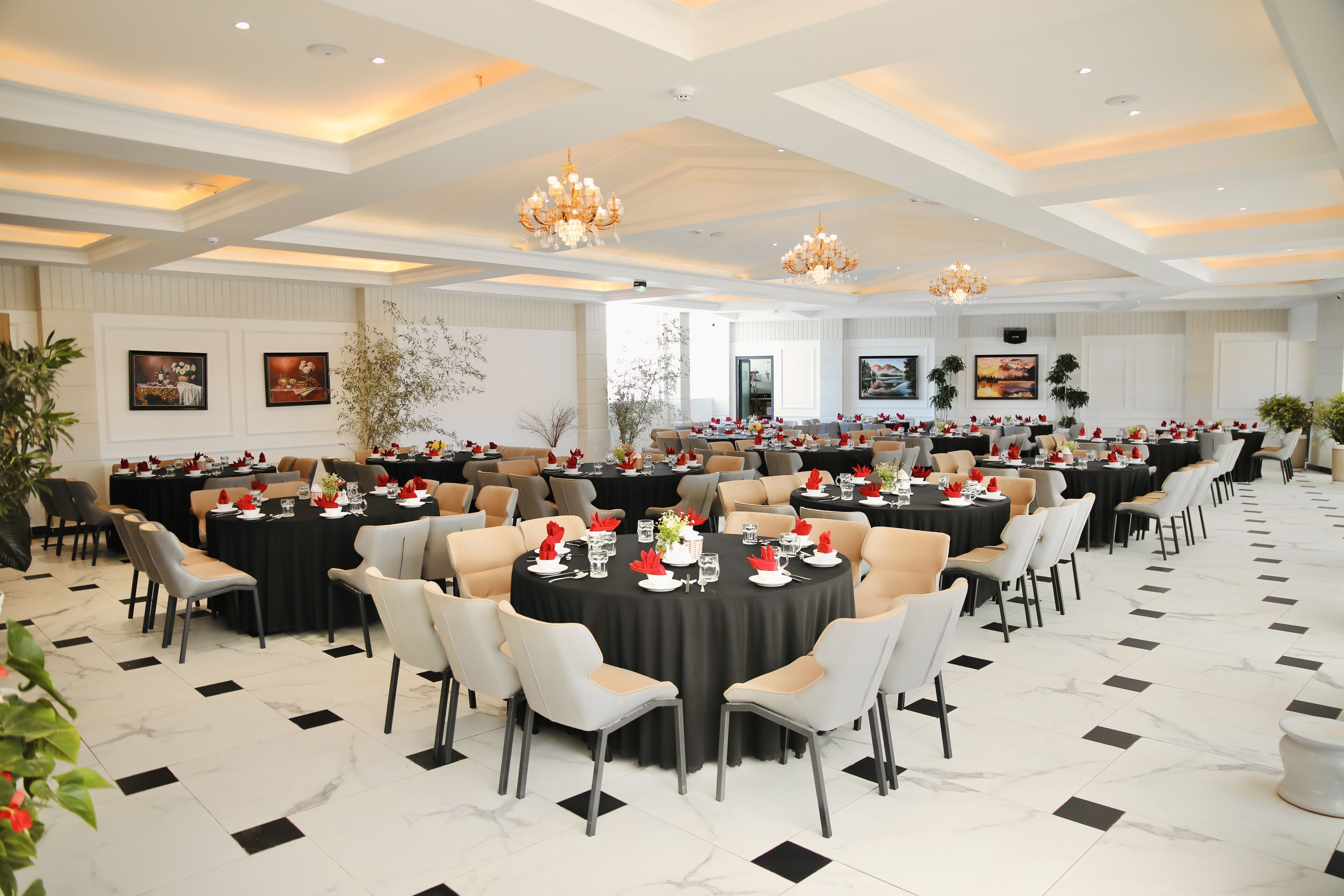 A spacious banquet hall with round tables, chairs, and chandeliers.