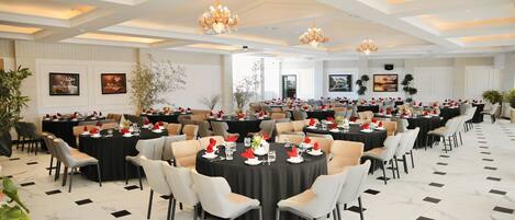 A spacious banquet hall with round tables, chairs, and chandeliers.