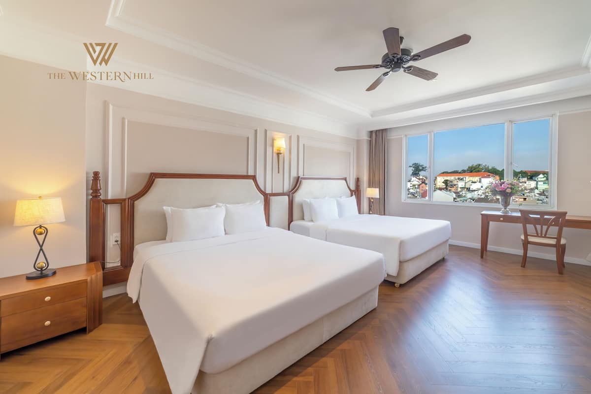A hotel room with two beds, a desk, a chair, and a view of the city.