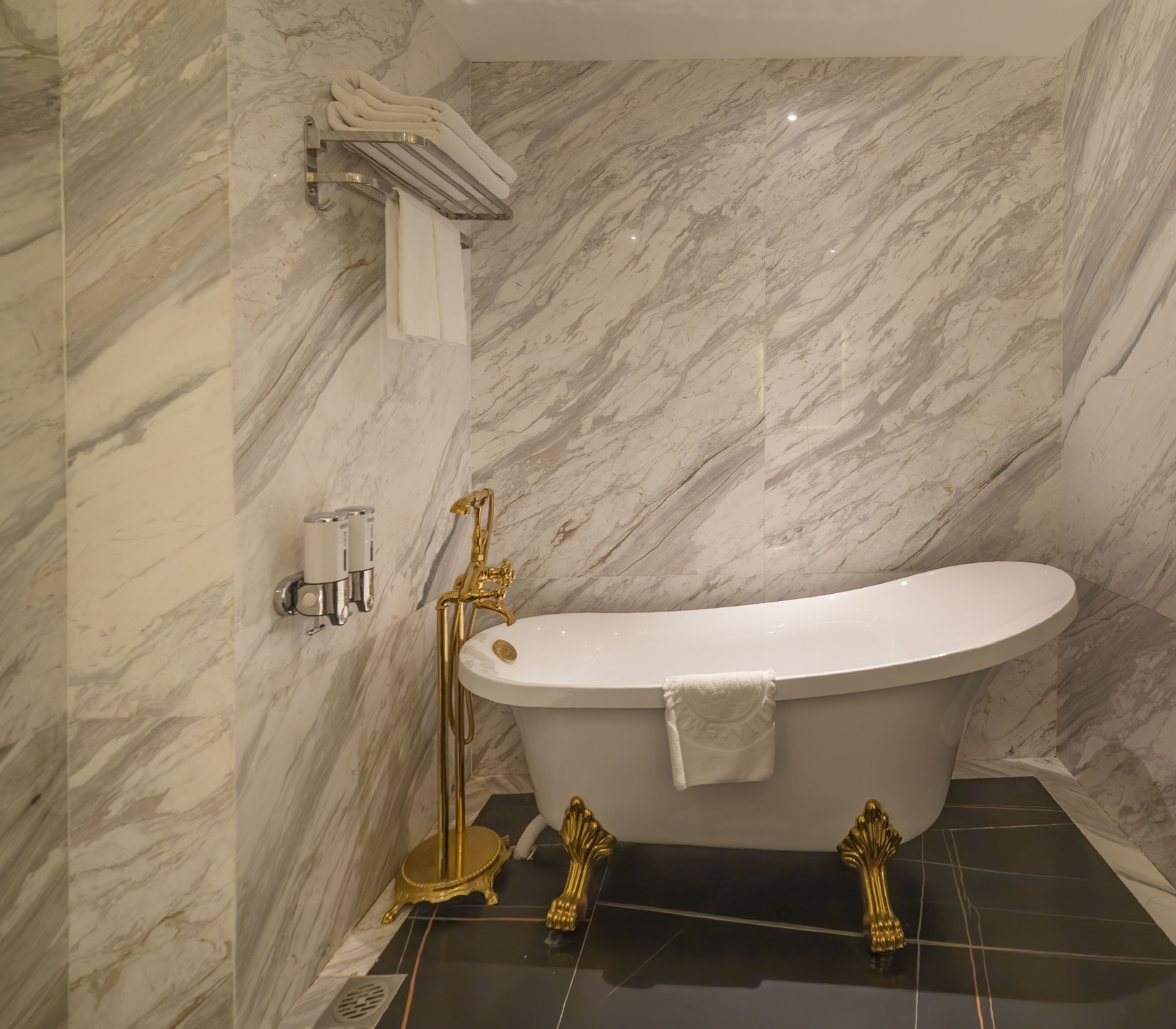A bathroom with a freestanding bathtub, marble walls, and gold fixtures.