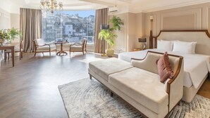 Habitación de hotel con una cama grande, un sofá, una mesa de comedor con sillas y vistas a la ciudad.