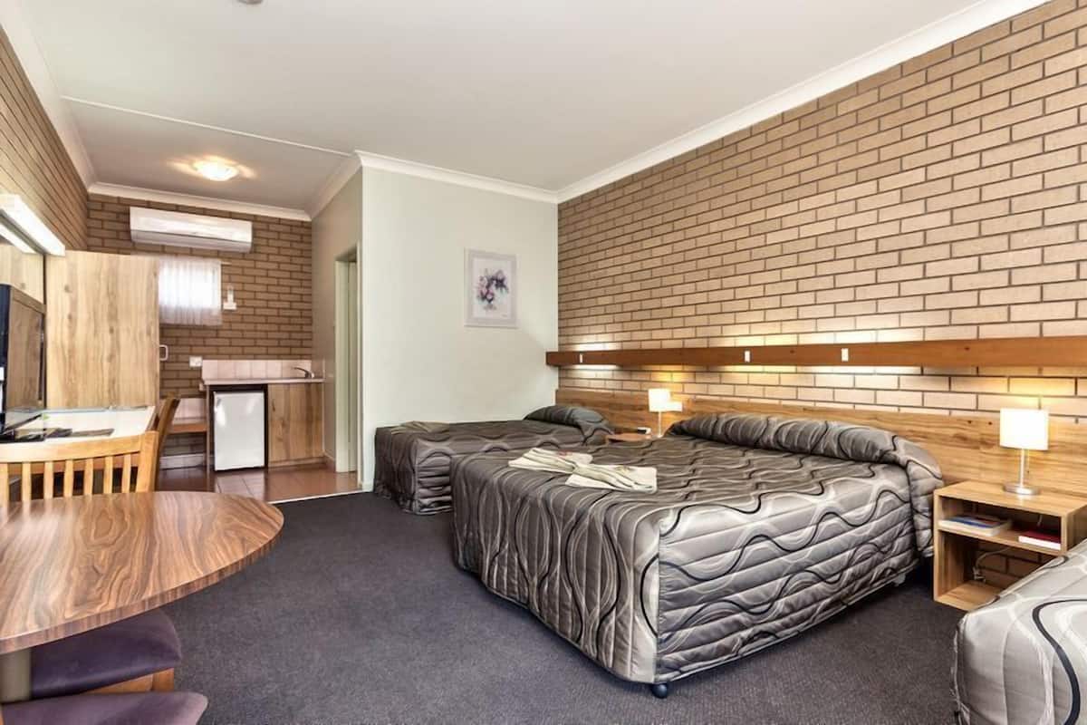 A modern hotel room with two beds, a wooden desk, and a kitchenette.