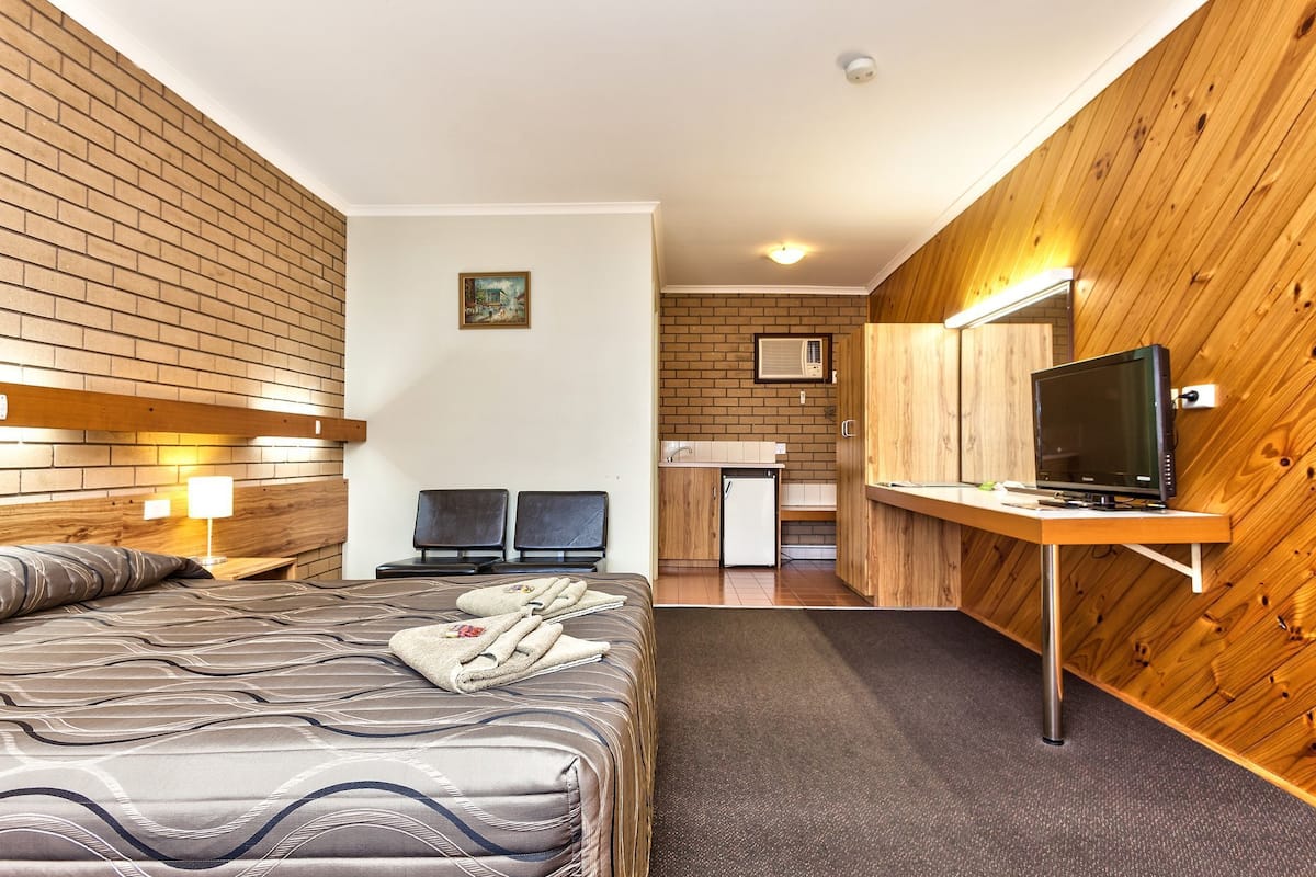 A hotel room with a bed, a desk with a computer, a small kitchenette, and a TV.