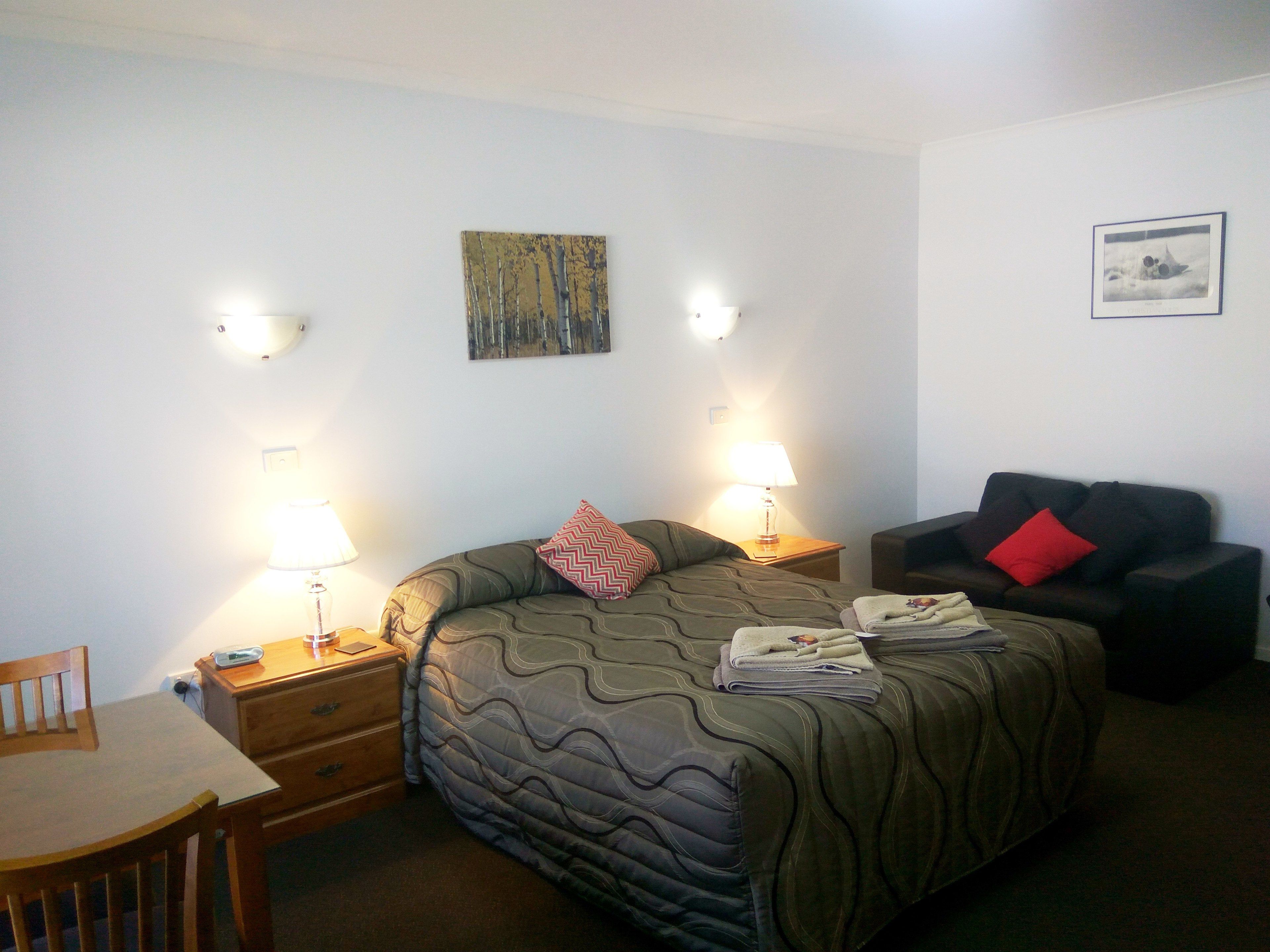 A hotel room with a bed, a desk, a chair, a sofa, and two wall-mounted lamps.